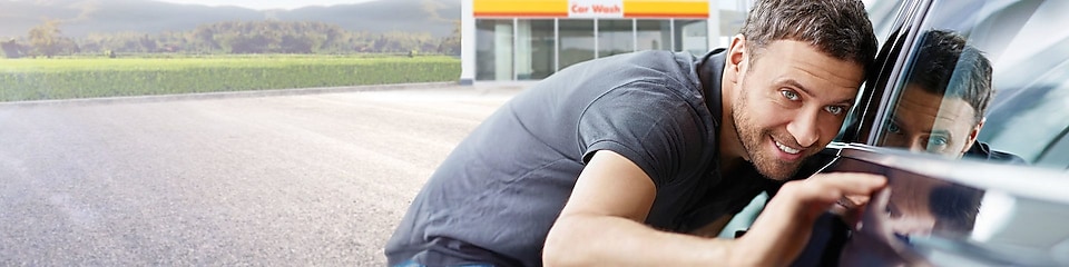 Ein junger Mann bewundert sein sauberes Auto vor  einer Shell Car Wash Station