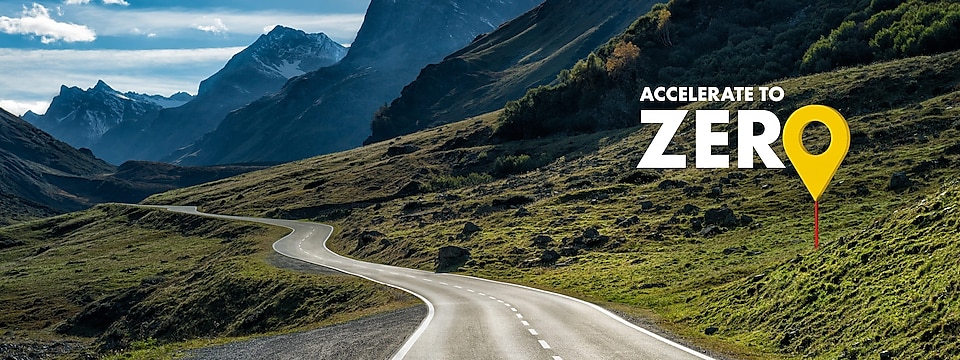 Eine Straße durch die Berge mit dem Accelerate to Zero Logo