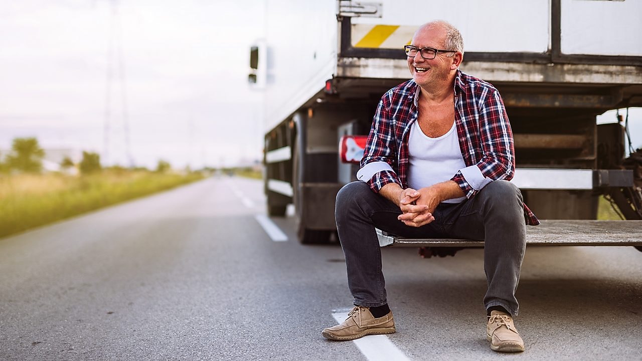 Ein Lkw Fahrer sitzt auf dem Heck seines Lkw.