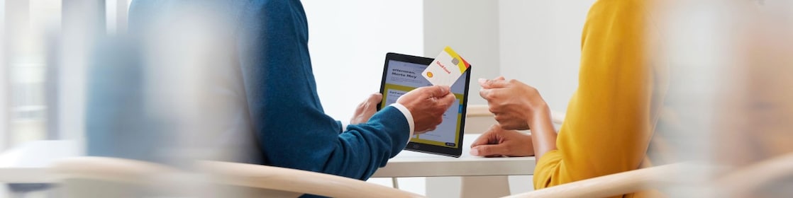 Ein junger Mann übergibt in einem Büro eine Shell Card an eine junge Frau.