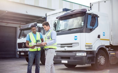 Zwei Fuhrpark-Mitarbeiter blicken vor einem Lkw auf ein Tablet.
