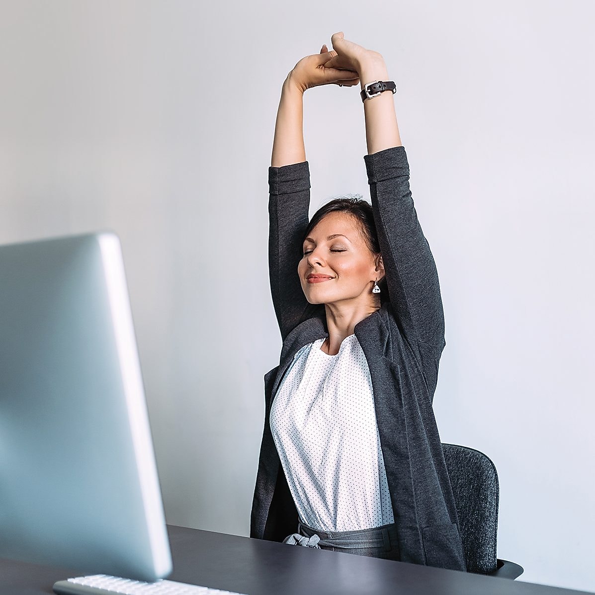 Frau sitzt am Computer und streckt sich.