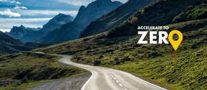 Auto fährt auf einer Schnellstraße durch grüne Landschaft mit Bergen im Hintergrund, Textaufschrift: "Accelerate to Zero".