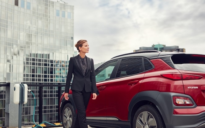 Eine Frau steht neben ihrem E-Auto.