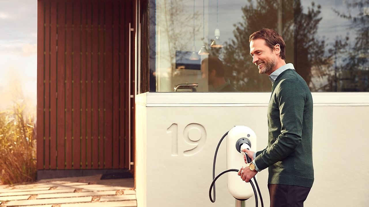 Lächelnder Mann vor einer Ladestation zu Hause