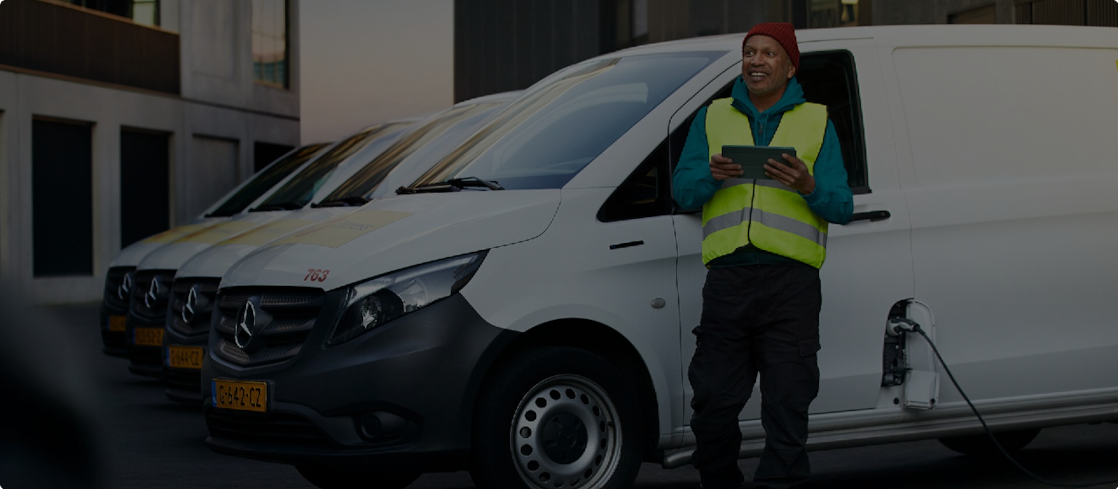 Ein Mann steht mit einem Tablet in der Hand vor mehreren E-Transportern, die aufgeladen werden