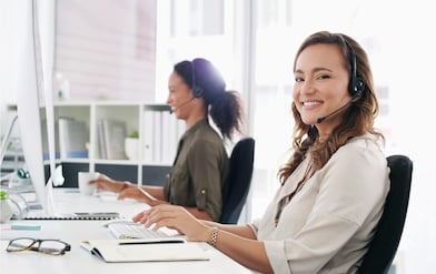 Eine Frau mit Headset blickt in die Kamera und lächelt.
