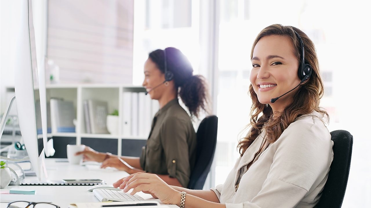 Eine Frau mit Headset blickt in die Kamera und lächelt.