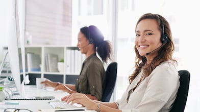 Eine Frau mit Headset blickt in die Kamera und lächelt.