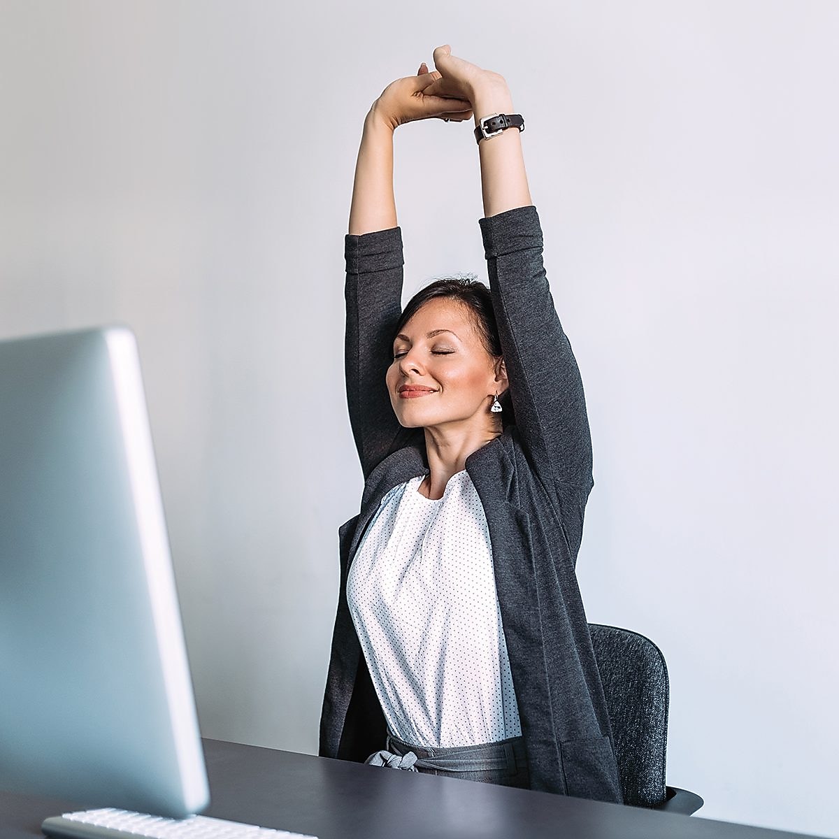 Frau sitzt am Computer und streckt sich.