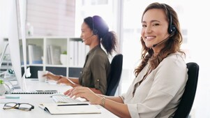 Eine Frau mit Headset blickt in die Kamera und lächelt.