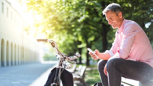 Ein Flottenmanager sitzt entspannt auf einer Parkbank mit seinem Smartphone in der Hand. Davor steht sein Fahrrad.