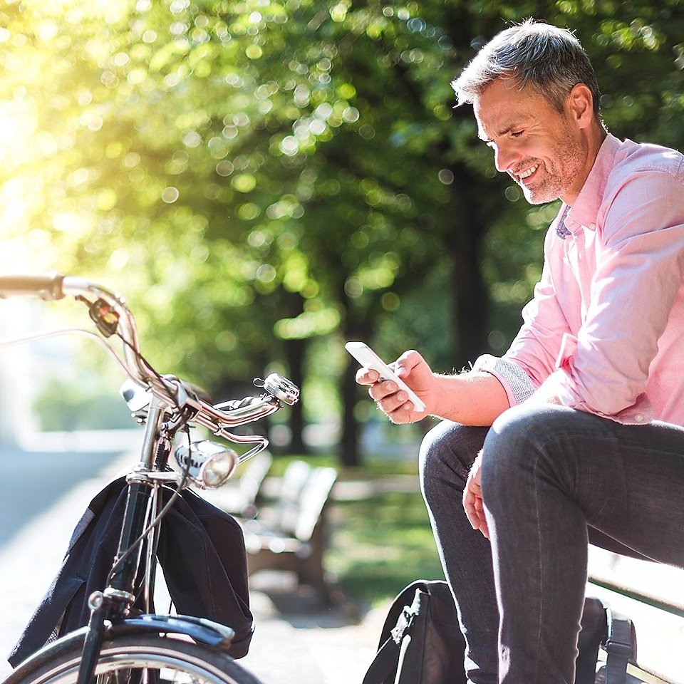 Ein Flottenmanager sitzt entspannt auf einer Parkbank mit seinem Smartphone in der Hand. Davor steht sein Fahrrad.