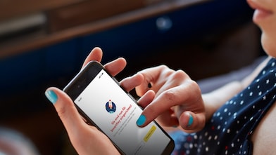 Frau sitzt im Auto und hält in der Hand ein Handy mit geöffneter Shell App und fertig eingerichtetem Shell SmartPay