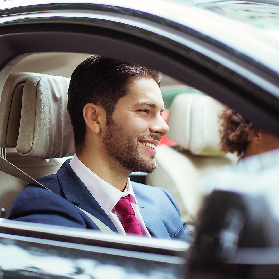 Lächelnder Mann auf Beifahrersitz eines Autos, durch die offene Scheibe fotografiert