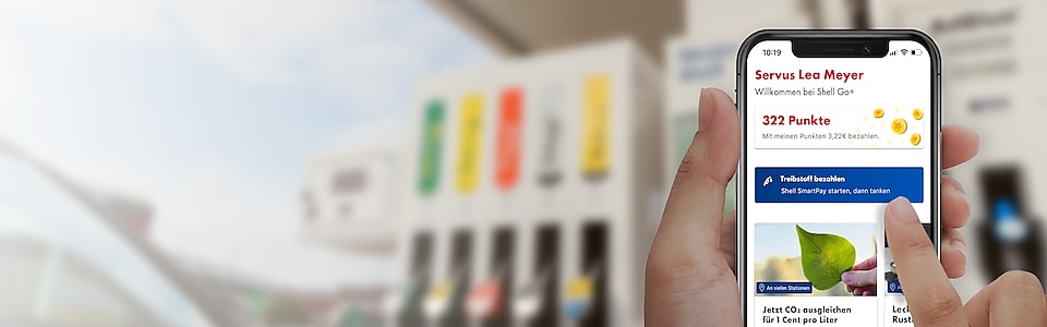 Shell App Startbildschirm auf Handy mit Tankstelle im Hintergrund
