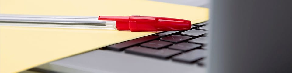 Roter Kugelschreiber und gelbes Blatt Papier auf der  Tastatur eines Laptops