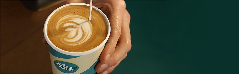 Barista schenkt Milchkaffee in einen Shell Café Becher ein