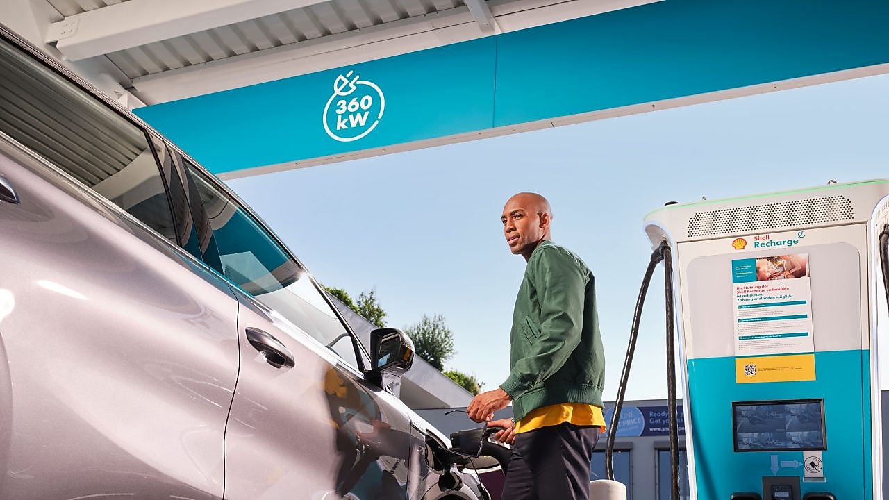Lächelnde Frau lädt ihr E-Auto an einer Shell Recharge Ultraschnell-Ladesäule