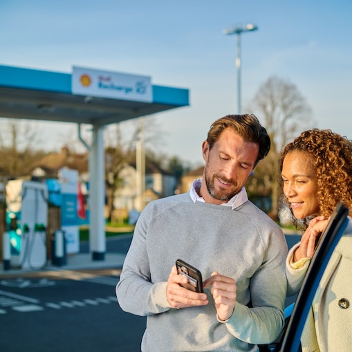 Zwei Personen mit Smartphone vor einer Shell Recharge E-Ladestation.