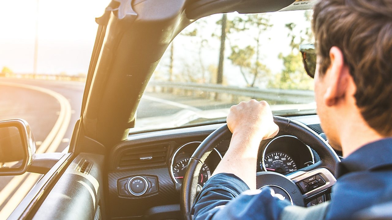 Junger Mann mit Sonnenbrille fährt im Cabrio der Sonne entgegen