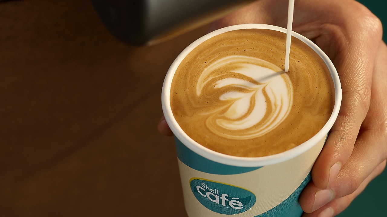 Barista schenkt Milchkaffee in einen Shell Café Becher ein
