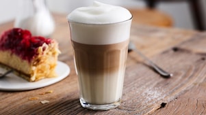 Latte Macchiato von Shell Café in einem hohen Glas auf einem Holztisch.